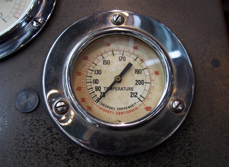 close up of an old round metal temperature gauge with the meter reading in Fahrenheit and Celsius...
