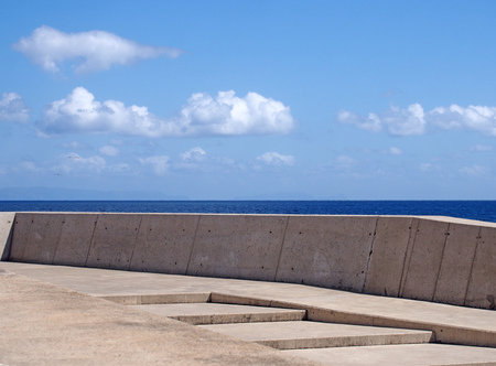 Concrete sea wall with steps against a calm blue sea and sunlit blue skyの写真素材