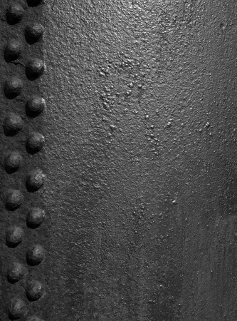 Old black rough iron metal surface with grainy texture and lines of rivetsの写真素材
