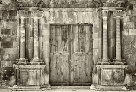 Monochrome sepia ancient wooden double doors in an old stone building with crumbling ornate columns surrounding the entranceの写真素材