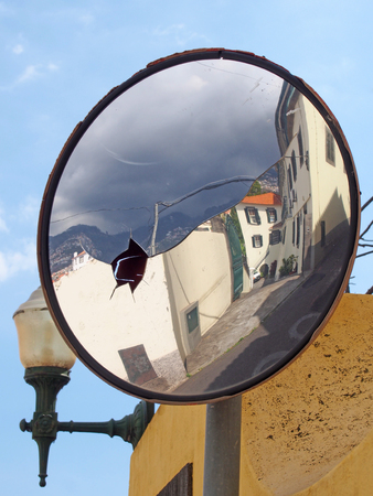 Street of old traditional houses in funchal madeira reflected in an old cracked traffic mirror against a blue skyの写真素材