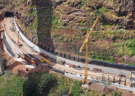 aerial view of a new road under construction with crane and construction materials and machinery working on the site with a tunnel being excavated through the landscape in funchal madeiraの写真素材