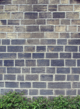 an old sandstone wall with large bricks with a row of plants and pink flowers alone the bottomの写真素材
