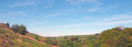 a long panoramic view of west yorkshire countryside with fields and moors above the woodland in hardcastle crags with a blue sunlit cloud skyの写真素材