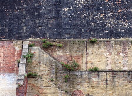 full frame image of a very large old brick wall with many patched and repaired sections stains weeds and black painted areaの写真素材