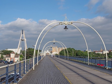 southport, merseyside, united kingdom - 28 july 2019: the historic pier in southport merseyside with people walking towards the town and the suspension bridge and buildings visible behind treesのeditorial素材