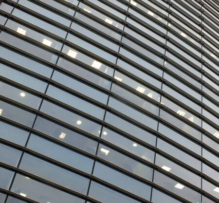 illuminated windows on the facade of a large curved modern office building with lights turned on on...