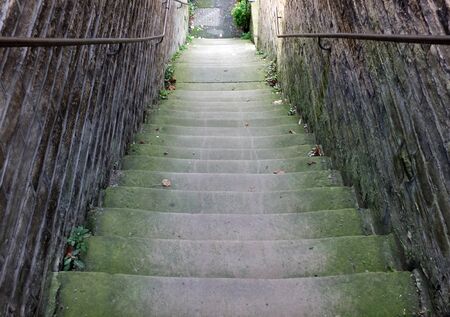 a perspective view of narrow old outdoor stone steps descending between walls with weeds and moss growing in the cornersの写真素材