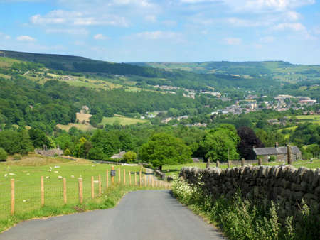 country lane running downhill surrounded by fields with sheep with a view of the town of mytholmroyd surrounded by woods and fields in the calder valley west yorkshireの写真素材