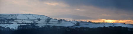 panoramic view of a glowing orange sunset in a cloudy twilight winter sky with snow covered fields...