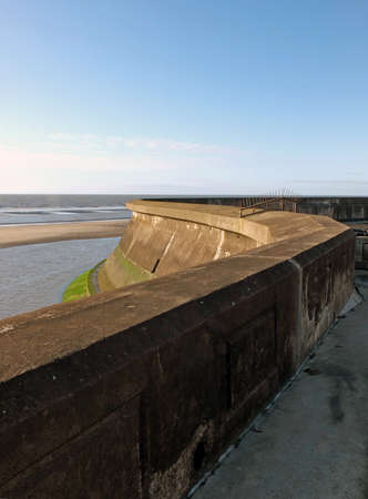 view of the concrete seawall in the cliffs area blackpool with the beach and incoming tide in sunlight with the outs wall of the old boat poolのeditorial素材