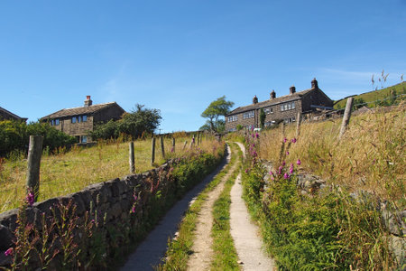 narrow country lane going up a hill in scenic west yorkshire countryside with stone houses near...