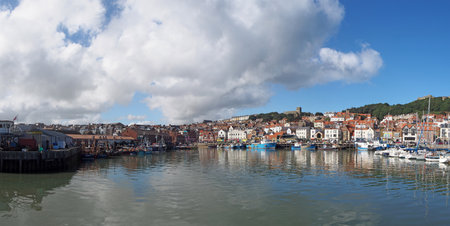 Scarborough, North Yorkshire, United Kingdom - 10 September 2022: long panoramic view of the harbour in scarborough on a summer day with fishing boats reflected in the water and town buildingsのeditorial素材