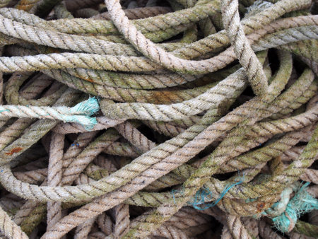 old worn brown coiled and knotted marine fishing rope with frayed ends stained by the seaの写真素材