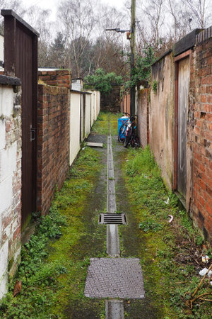 typical narrow back alley in an english city street with brick back yard walls and rubbish on the ground and a bicycle against a wallの写真素材