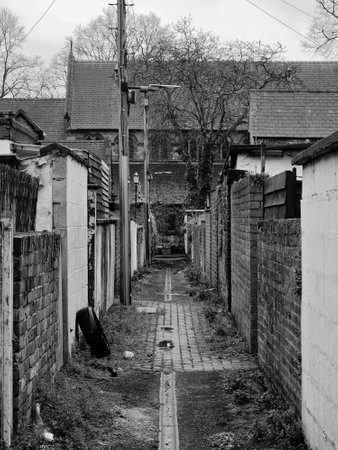 typical narrow back alley in an english city street with brick back yard walls and rubbish on the groundの写真素材