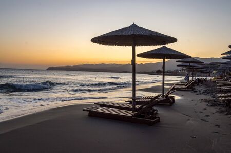 Sunbeds and umbrellas at sunrise on Stalis beach in northern Creteの写真素材