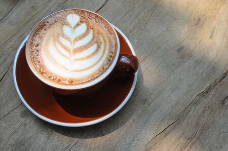 Cappuccino coffee in a brown coffee cup. Placed on a wooden tableの写真素材