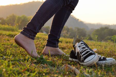 Woman take off ones sneakers and walking through a meadow with lush grass