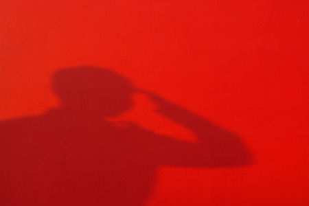 Shadow Proud saluting male army soldier on red backgroundの写真素材