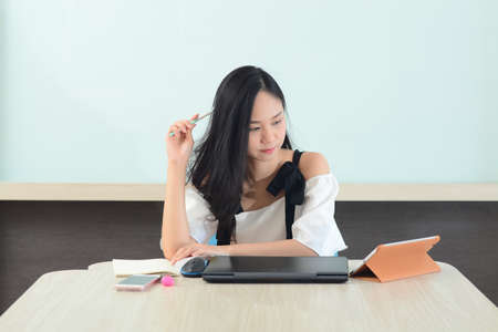Asian woman analyzing work with laptop and books in office