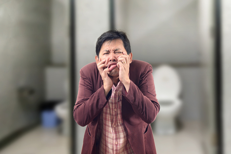 Asian Businessman feel pain with constipation and crumpled face in front of the bathroomの写真素材