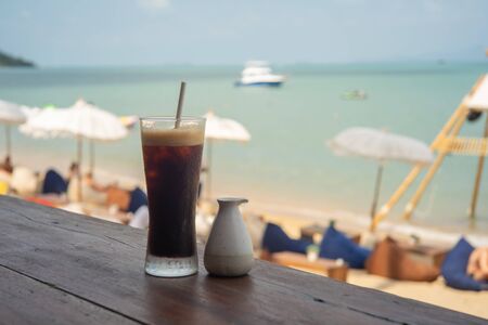 Cold black coffee and syrup over terrace wood with beach and sea backgroundの写真素材