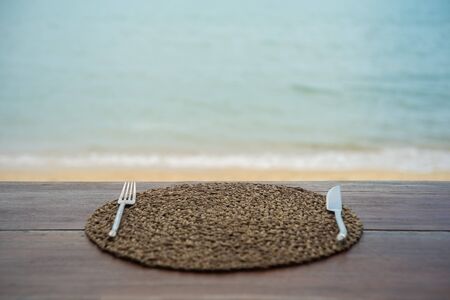 Defocus and blur image of knife and fork over water hyacinth tray on terrace wood with beach and sea blur background.の写真素材
