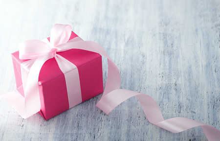 Pink gift box with ribbon on white painted wood background