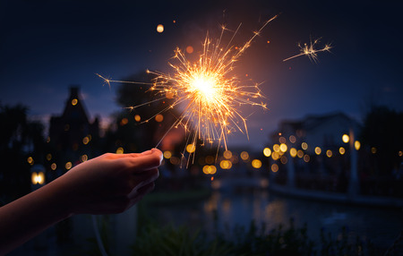 Hand holding a sparkler with neighborhood backgroundの写真素材