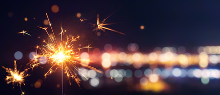 Glittering burning sparkler against blurred bokeh light backgroundの写真素材