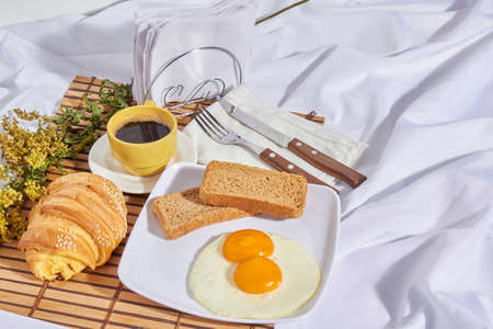 American breakfast in bed with whole fried eggs, toast, red wine, chocolate, cheese and bread with...