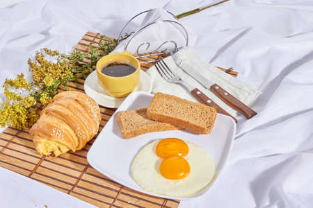 American breakfast in bed with whole fried eggs, toast, red wine, chocolate, cheese and bread with...