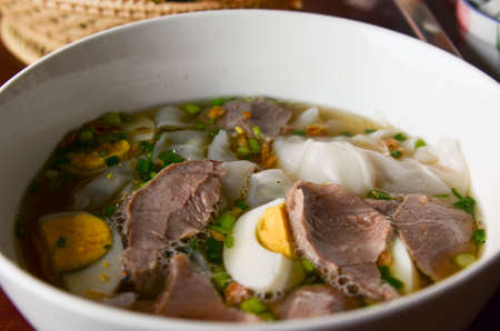 Closeup of a person eating Thai style crispy pork rice noodle soup from a bowl with chopsticks. Pineapple fried rice in the background.の写真素材
