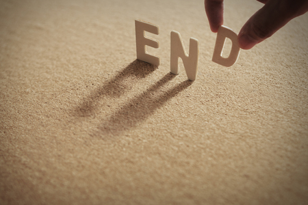 END wood word on compressed or corkboard with human's finger at D letter.の写真素材