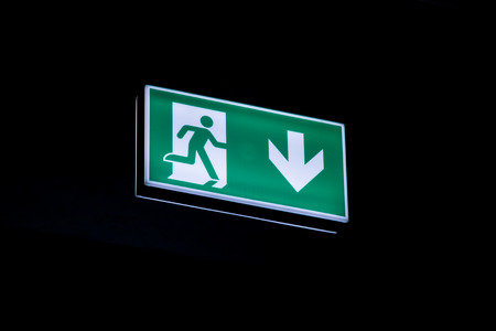 Exit sign hanging on the ceiling of a parking garage. In the dark illuminated green and white symbol.の写真素材