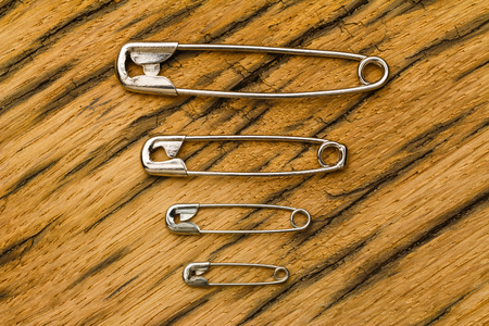 Small to big safety pins or needles of metal. On old oak wood usable as background.の写真素材