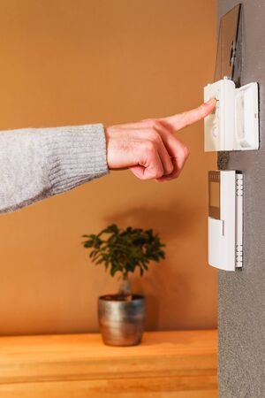 Young male hand pressing button of electronic appliance on wall of modern home. Clean background scene gray wool sweater.の写真素材