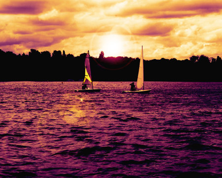 Two Boats race across a lake with sunset tones and lens flare の写真素材