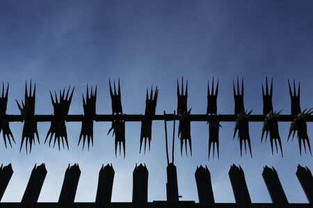 Silhouette of metal security fence from a low angle with blue sky background 