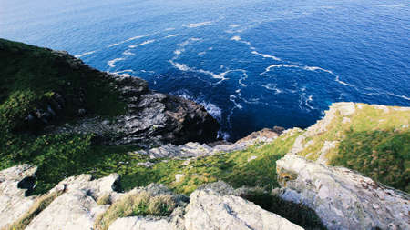 Cornish cliff side drop towards the sea, contrasting rock formations, plant life greens against the...