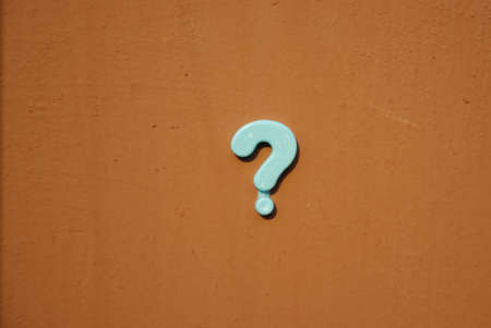 A question mark made of plastic on a painted brown background