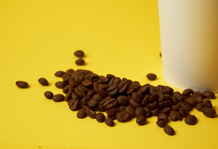 coffee beans next to a paper cup on a yellow backgroundの写真素材