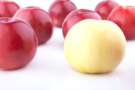 Yellow apple out of the red apples group on the white backgroundの写真素材