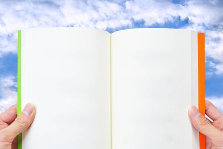 The hand is opening the book that on the sky backgroundの写真素材