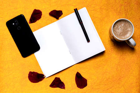 Flat-lay open note book on a yellow background with a mobile, pen and a cup with tea.
