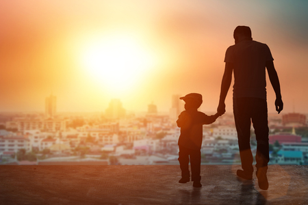Child, baby holding an adult's hand. Father and son on a walk. Happy lovely baby on a wooden terrace with sun sets blurred. Little baby having fun time activity .silhouette concept.の写真素材