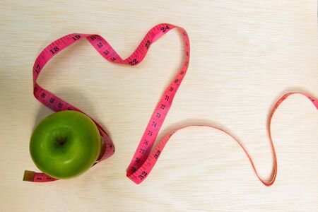 Closeup of green apple and pink tape wrapping around apple on aged wood table background healthy...