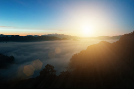 Natural fog and mountains sunlight background blurring, misty waves warm colors and bright sun light. Sky sunny color orange light patterns, abstract flare evening on clouds blur.の写真素材