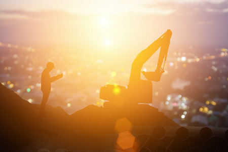 Silhouette excavator in construction site on sunset sky background and team of business engineers looking for blueprints in construction sites, through blurry at sunset in industryの写真素材